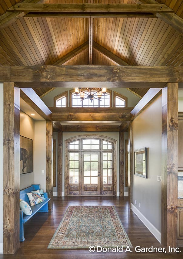 Interior view of a foyer with arched double doors, exposed timber beams, vaulted wood plank ceiling, and a chandelier.
