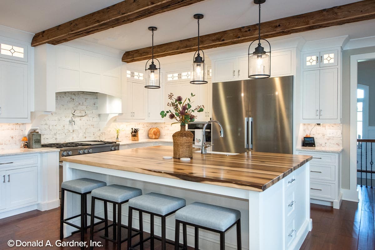 Kitchen with white cabinets, wood ceiling beams, large island with seating, and stainless steel appliances.