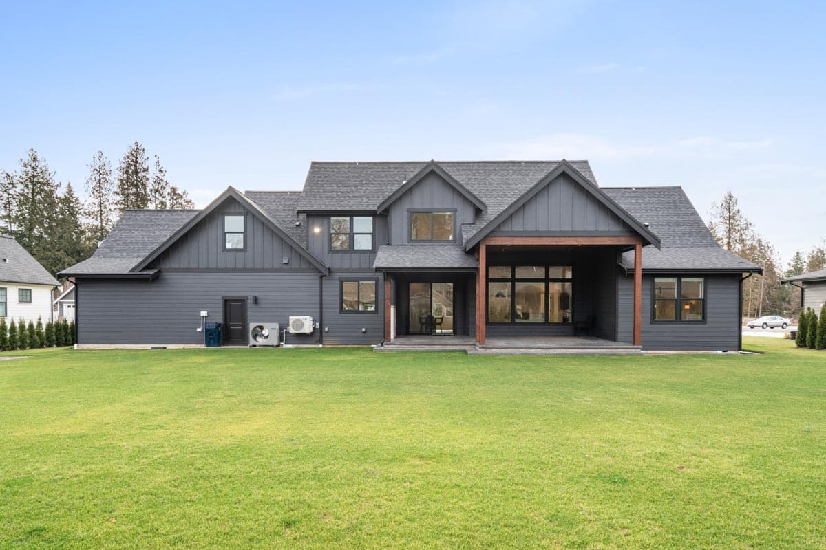 House plan exterior of a two-story modern home with dark siding, gables, dormers, and a covered patio.