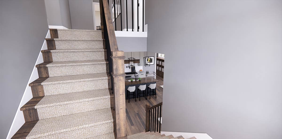 View from the top of a carpeted staircase leading to a kitchen with a dark island, white bar stools, and hardwood floors.