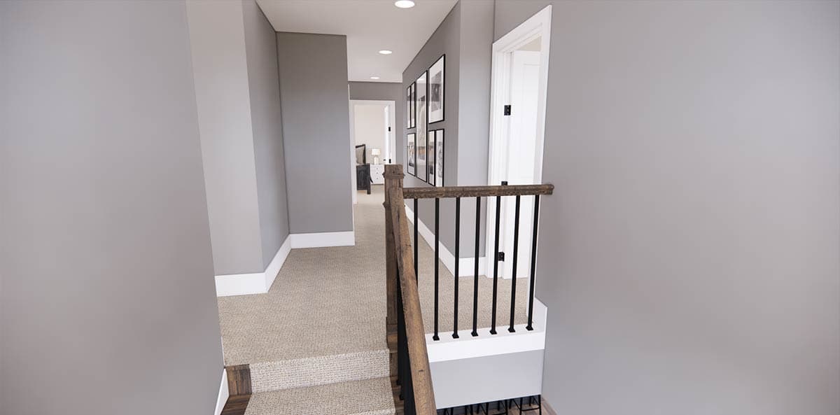 A hallway with gray walls, beige carpet, and a wooden handrail. Several framed pictures hang on one wall, leading to a doorway.