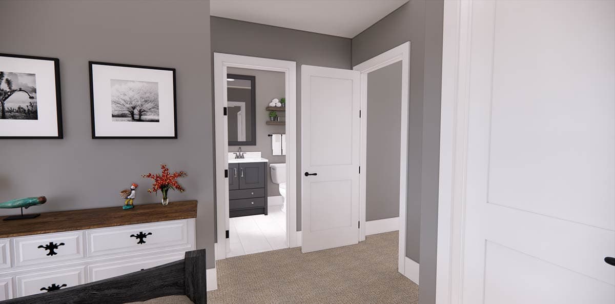 A bedroom interior features a chest of drawers with artwork and a view into a bathroom with a vanity and open door.