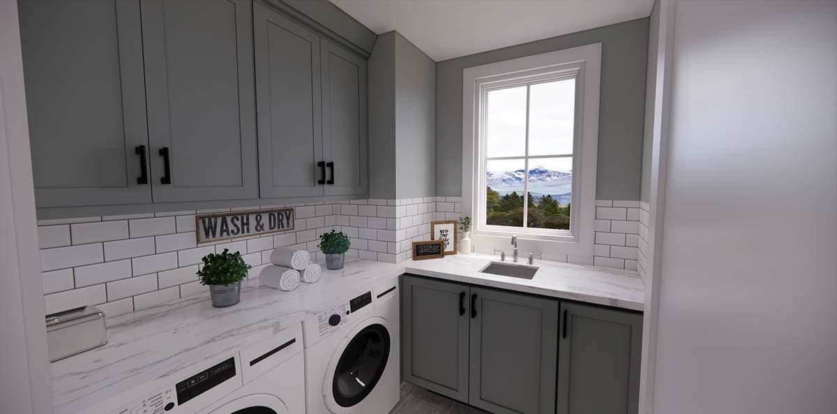 A modern laundry room with gray cabinets, white subway tile, and a washing machine. A window offers a scenic mountain view.