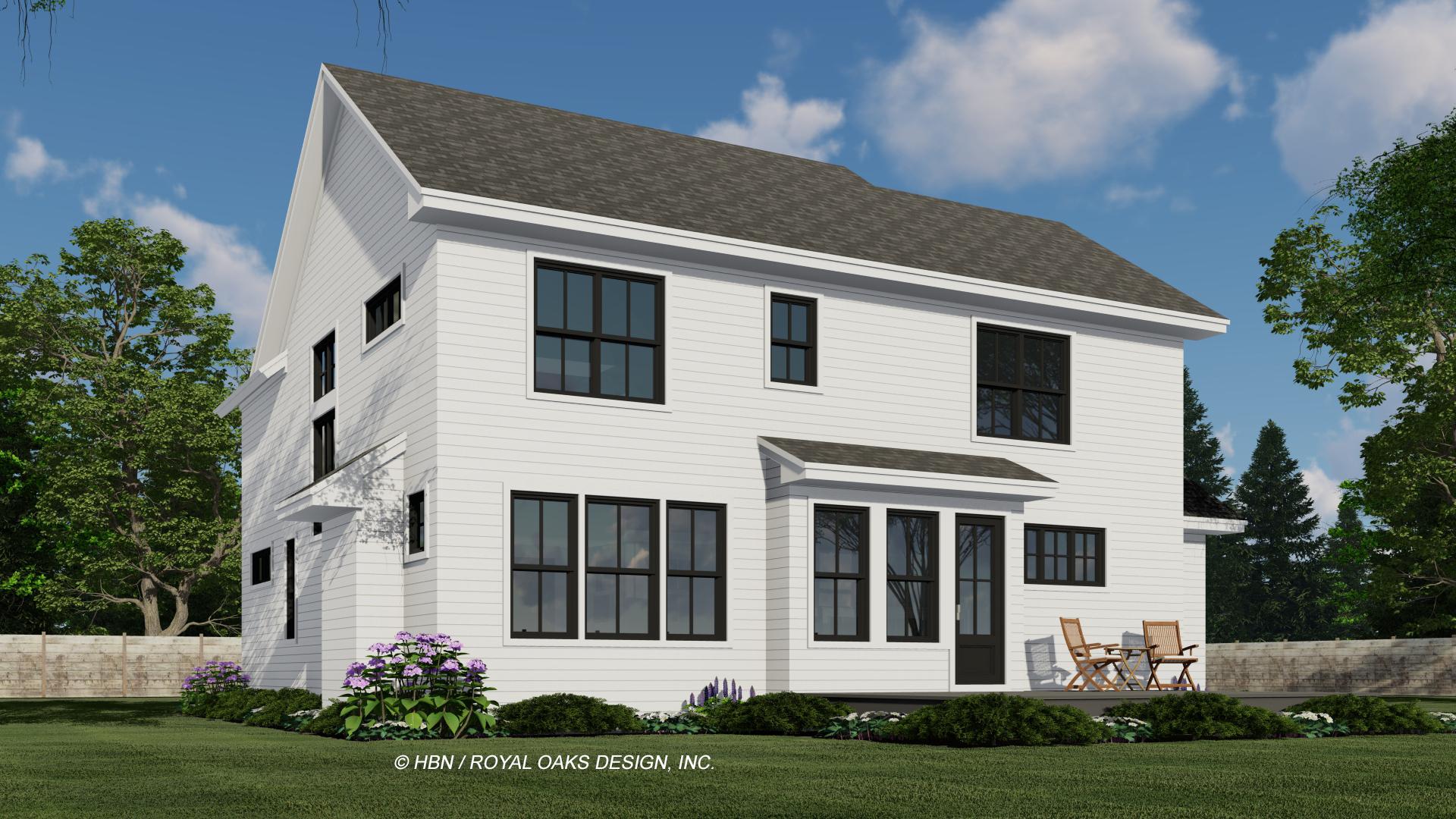 A modern white house with dark framed windows sits on a grassy lawn. The house features a prominent roof and a small deck with chairs.