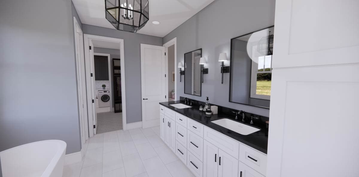 Modern bathroom with a double vanity featuring black countertops, white cabinets, and large mirrors. A laundry room is visible through a doorway.