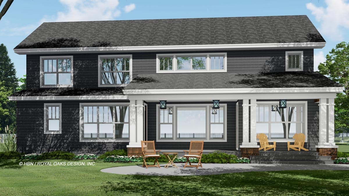 A two-story house with dark gray siding, white trim, and a covered porch. Two chairs and a small table sit on the patio.