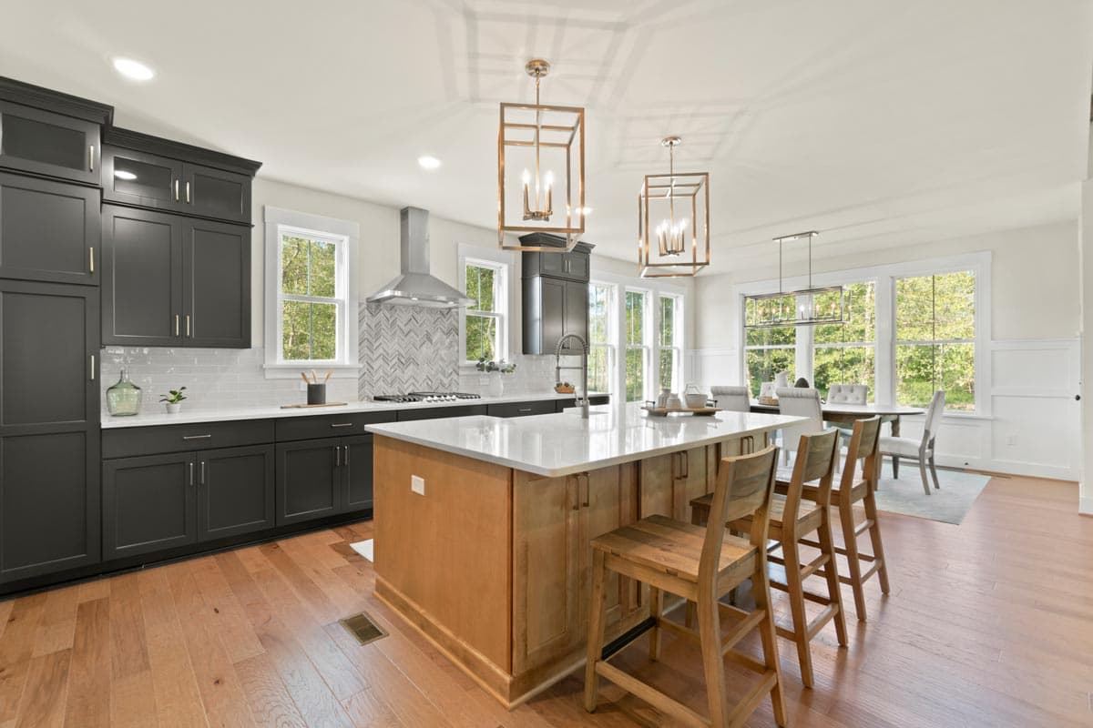 Kitchen with dark gray cabinets, white quartz countertops, and a light wood island with seating. Stainless steel range hood.