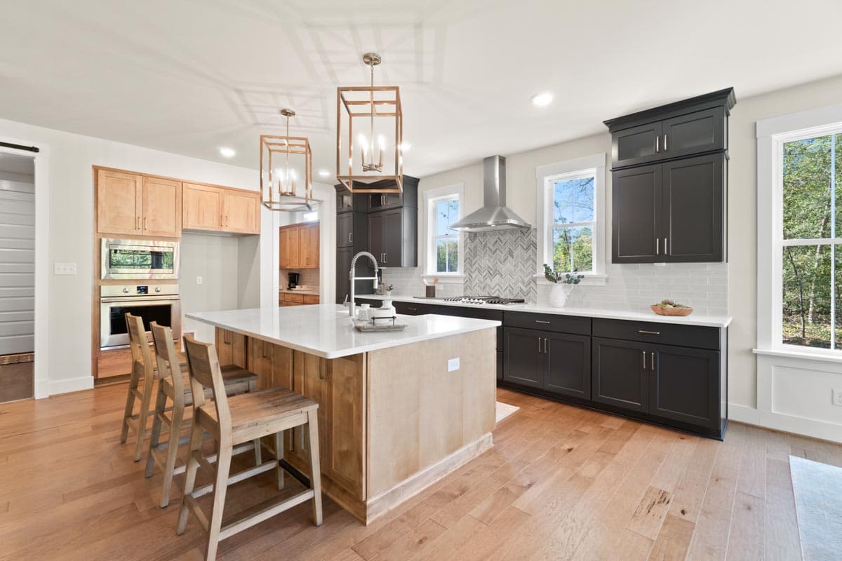 Kitchen with island, dark base cabinets, light wood upper cabinets, stainless steel range hood, and pendant lighting.