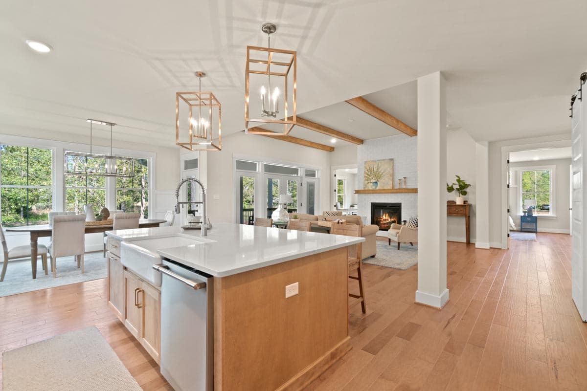 Interior view of an open-concept home with kitchen island, dining area, and living room featuring a fireplace and vaulted ceiling with beams.
