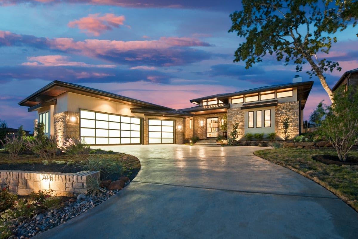 House plan exterior. Modern style, single story, with a flat roof, clerestory windows, and a two-car garage. Stone and stucco facade.