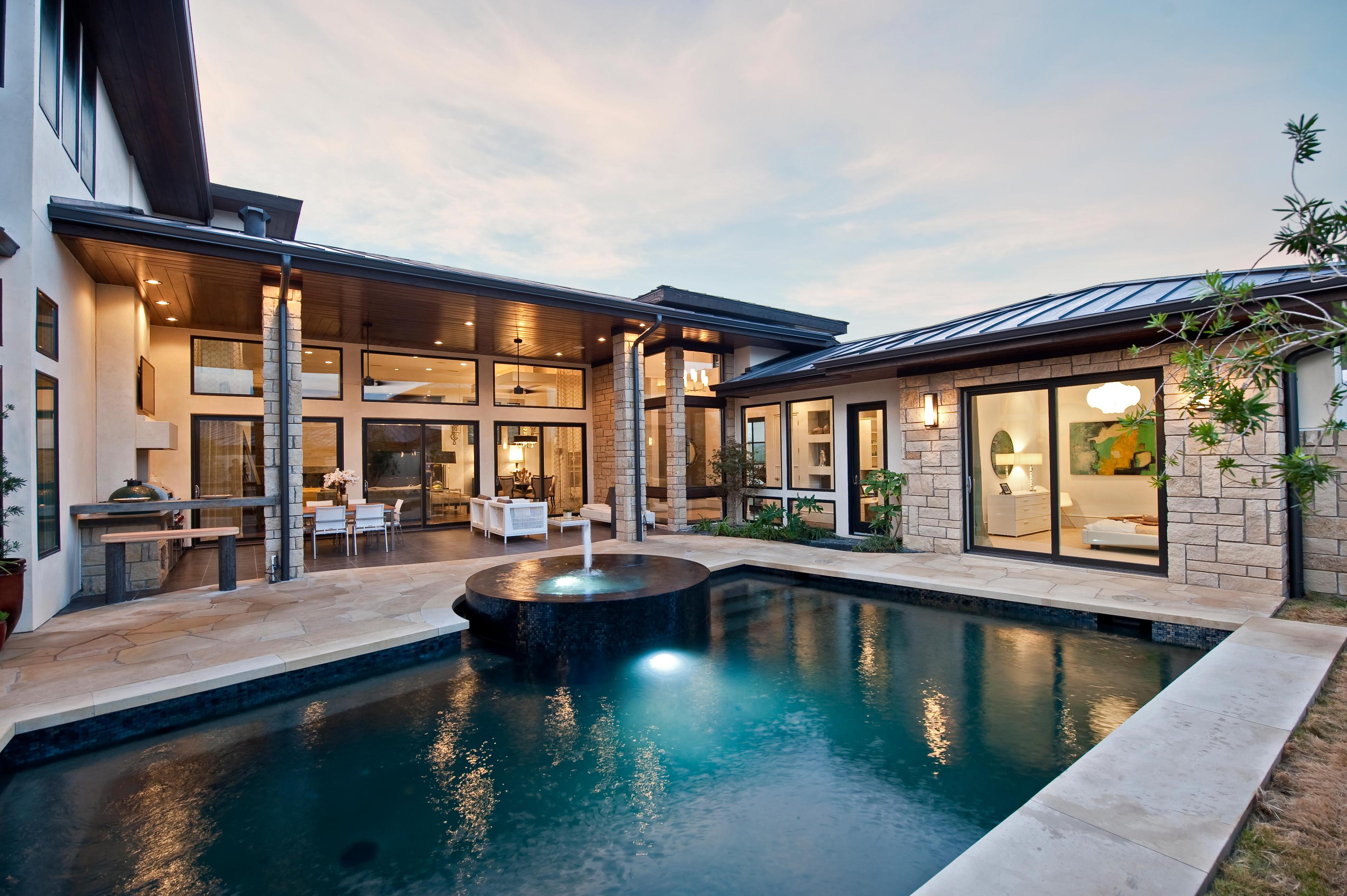 Modern house exterior with stone accents, flat rooflines, large windows, and an integrated pool with a fountain.