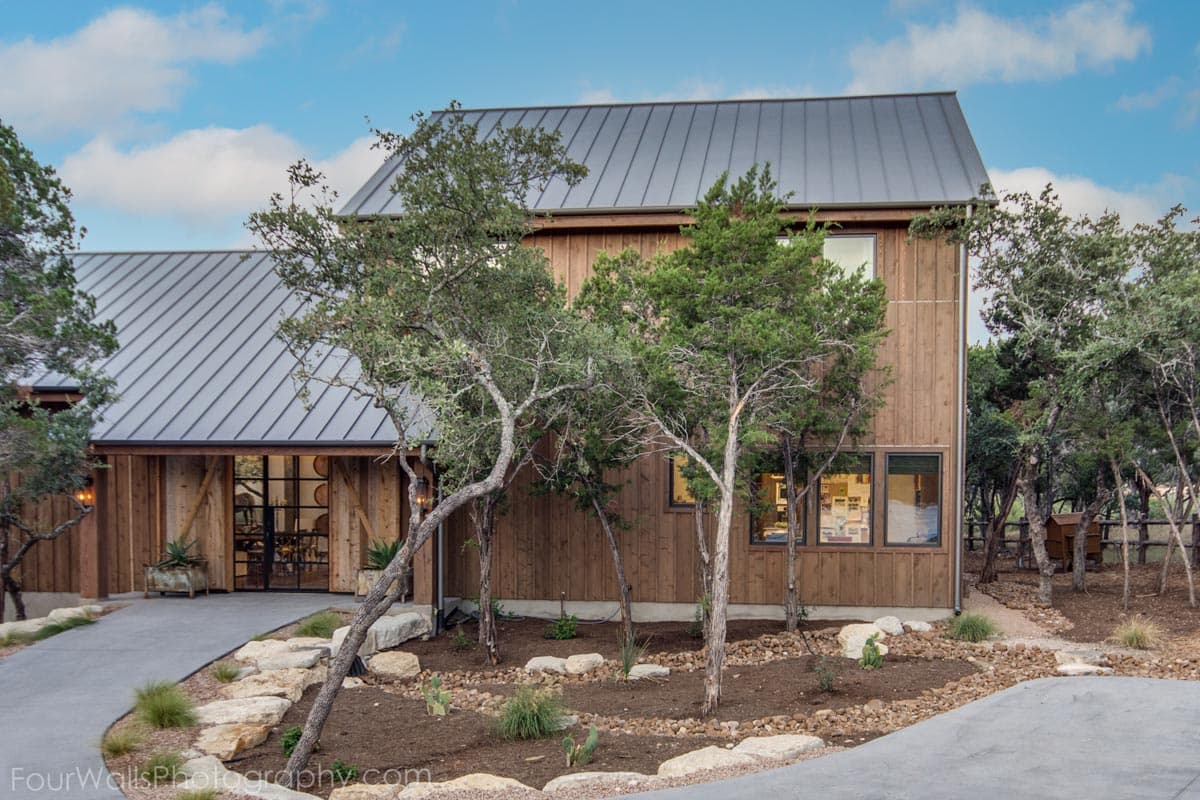 House plan exterior. Two-story, modern farmhouse style with a metal roof, board-and-batten siding, and large windows. Includes a concrete driveway.
