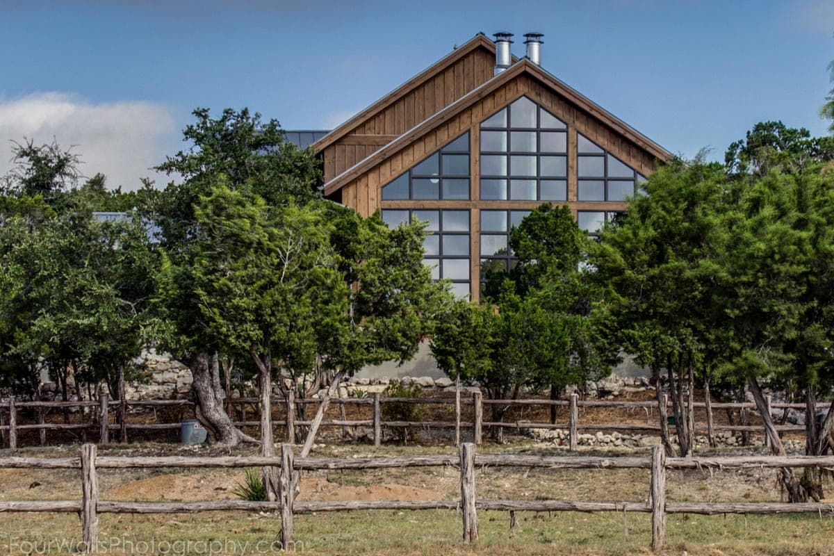 Modern house plan exterior with prominent gable end and expansive grid window wall. Wood siding and metal roof.