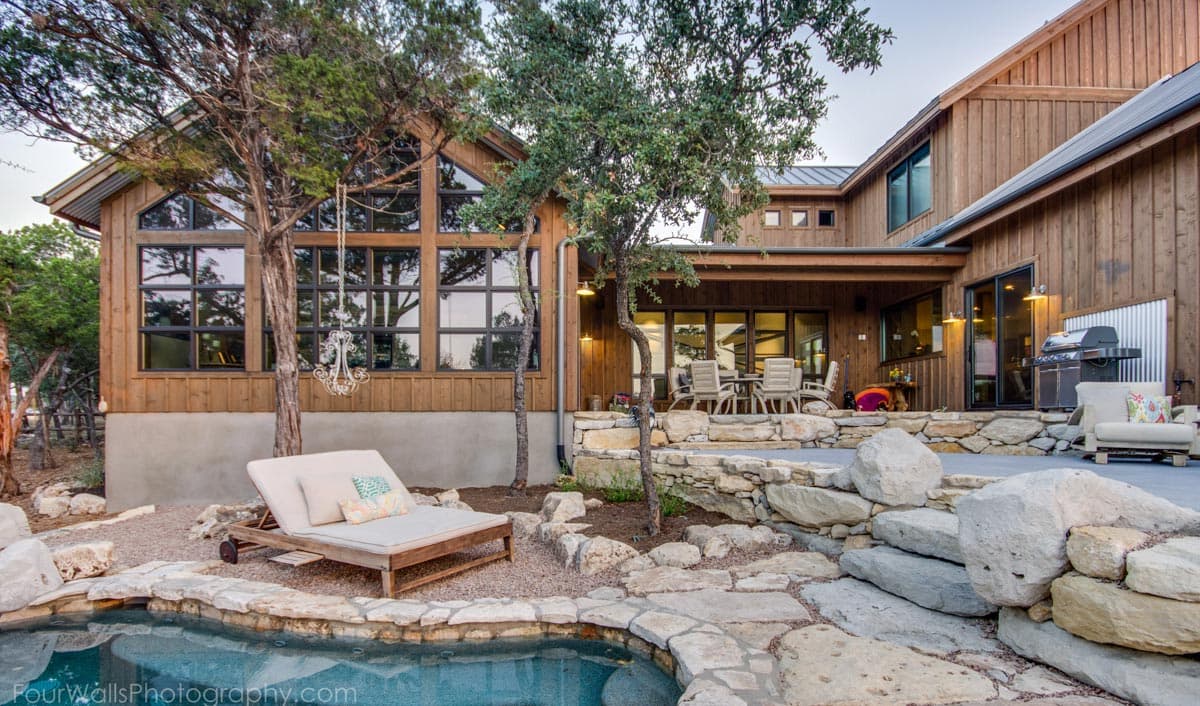 House plan exterior features wood siding, a metal roof, large gable windows, a covered patio, and a wraparound pool.