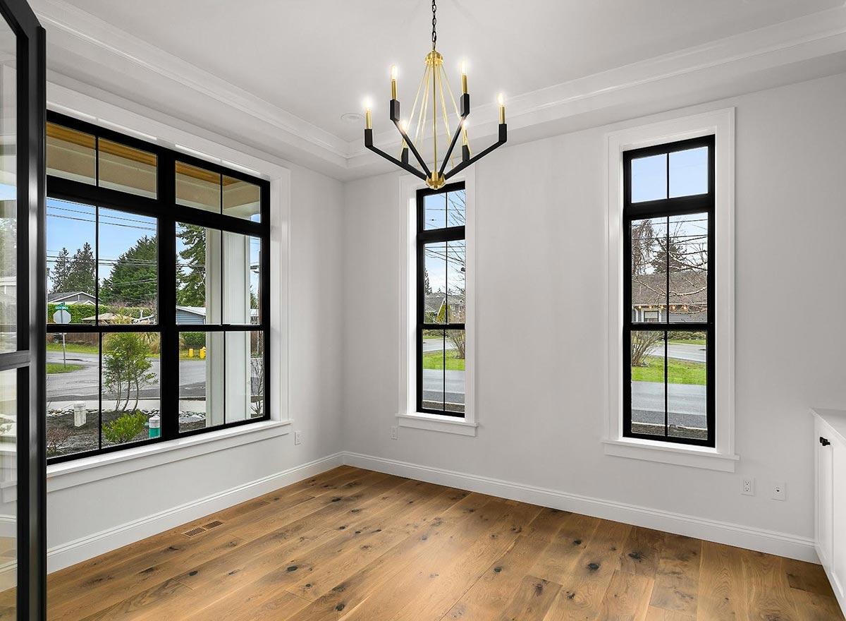 Interior view of a room with hardwood floors, large black-framed windows, and a contemporary chandelier.