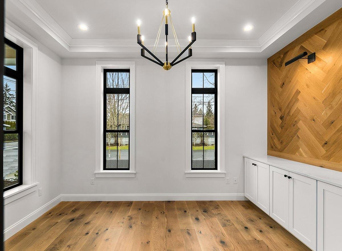 Interior view of a room with two tall windows, a modern chandelier, white built-in cabinets, and a herringbone wood accent wall.