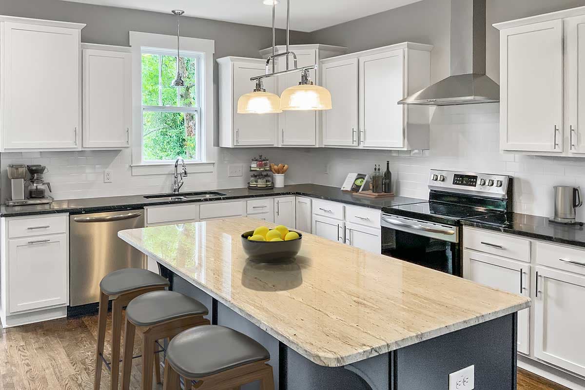 Kitchen interior with white cabinets, granite countertops, large island with seating, and stainless steel appliances.