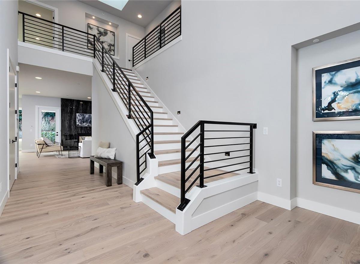 Modern staircase with open risers, white treads, and black horizontal railings in a multi-story foyer.
