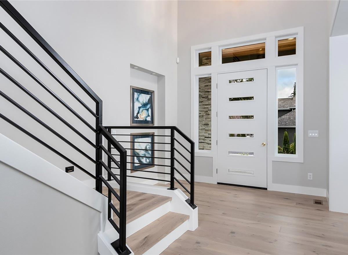 Modern house interior entrance with a white door featuring horizontal glass panes, a stone accent wall, and a staircase with black metal railings.