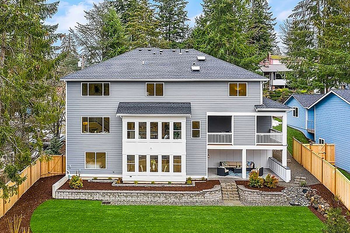 Two-story house plan exterior with gabled roof, multiple windows, covered porch, and lower-level patio.