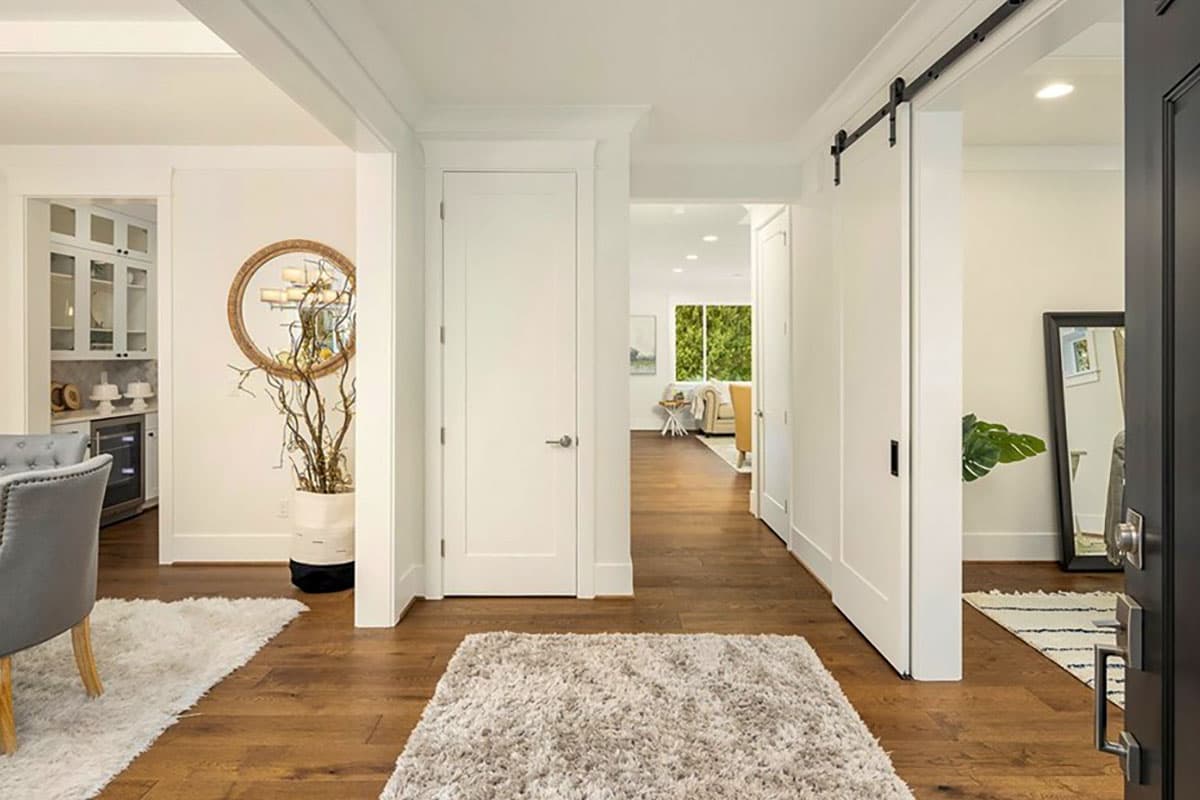 Interior view of a hallway with a barn door, a round mirror, and doorways leading to a kitchen and living area.