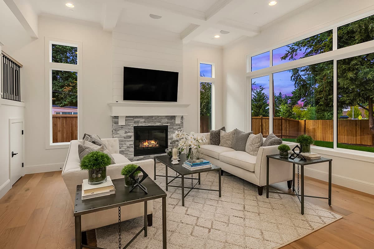 Interior view of living room with stone fireplace, coffered ceiling, and large windows showcasing an outdoor view.