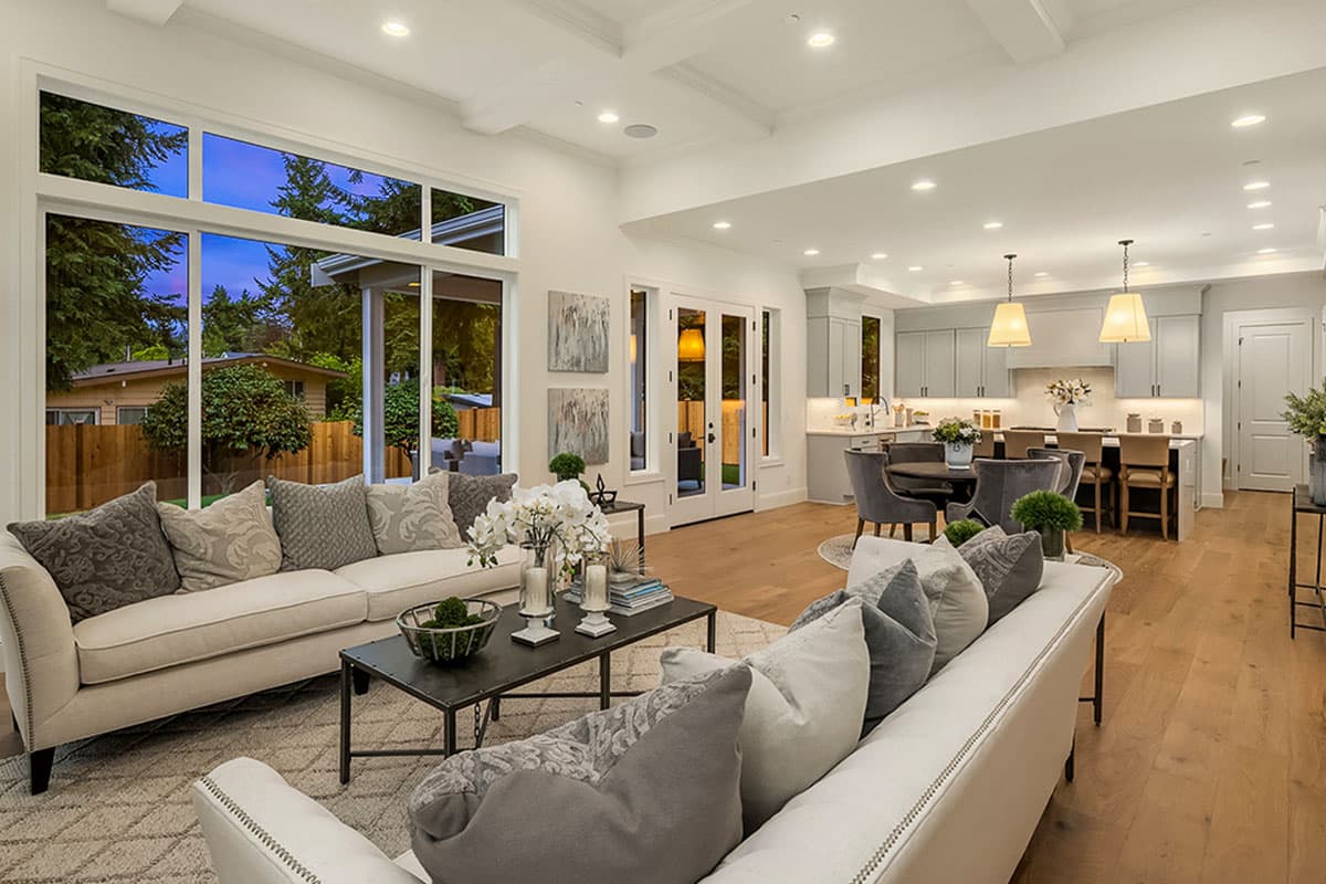 Open concept living area with large windows, coffered ceiling, and gray kitchen with island and pendant lights.