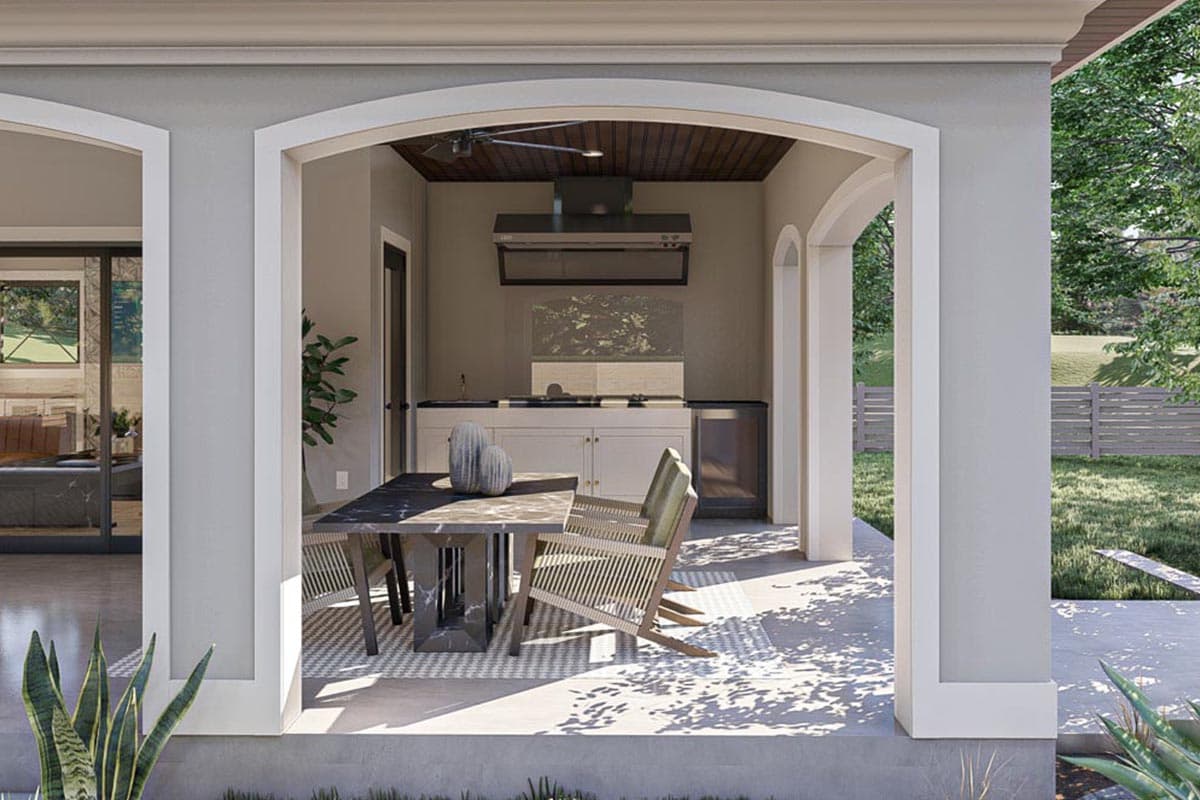Covered outdoor kitchen with grill, sink, and dining table under arched openings.