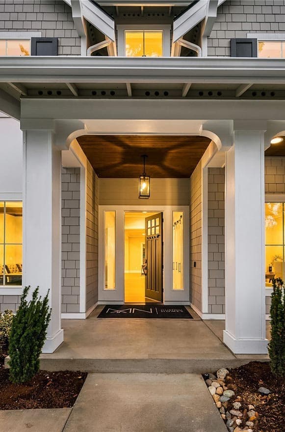House plan exterior with covered entry, wood plank ceiling, pendant light, glass-paneled door and flanking windows.