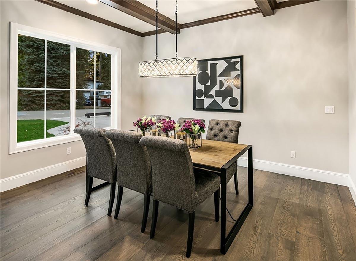Dining room with six upholstered chairs around a wood table, a modern chandelier, and a large window with a view of trees.
