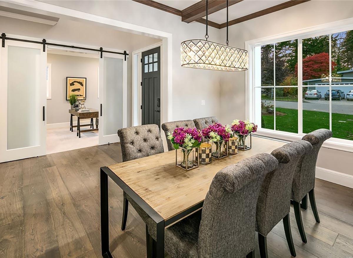 Dining room with wood floor, tufted chairs, glass pendant light, and barn doors leading to a home office.