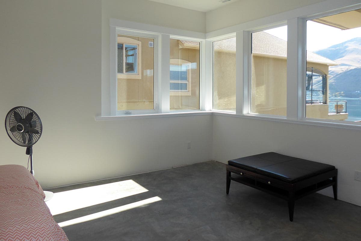 Interior view of a room with corner windows overlooking a body of water and mountains.