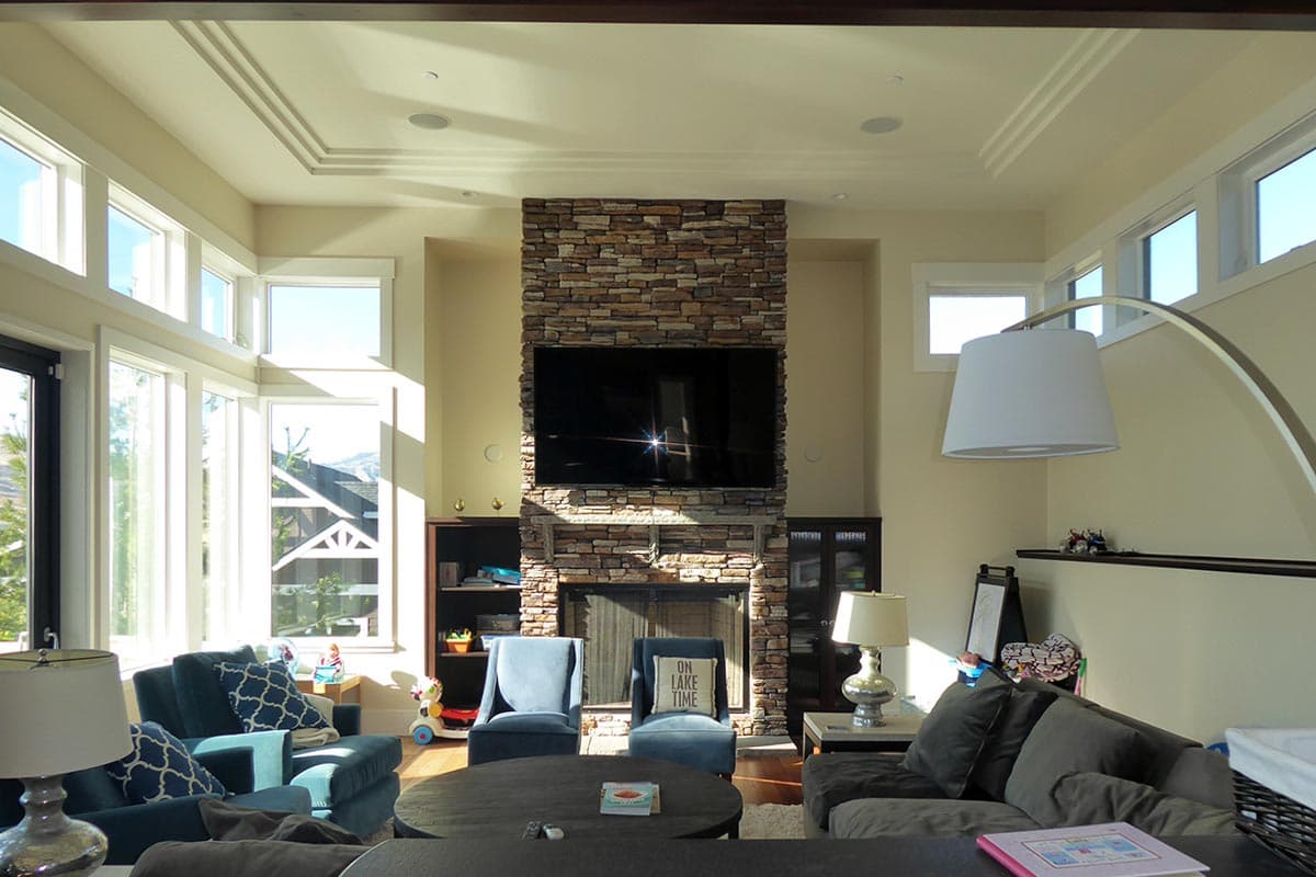 Living room featuring a stacked stone fireplace with mounted TV, coffered ceiling, and large windows.