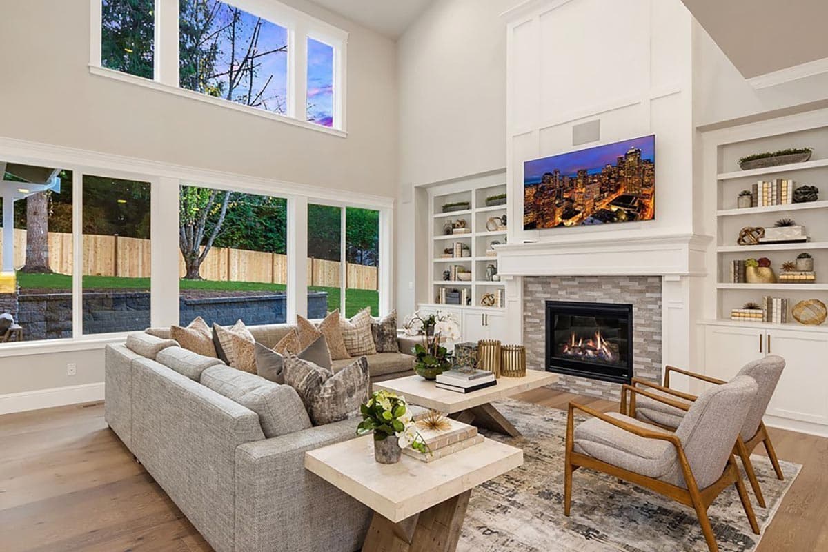 Living room with a vaulted ceiling, fireplace, built-in shelving, and large windows.