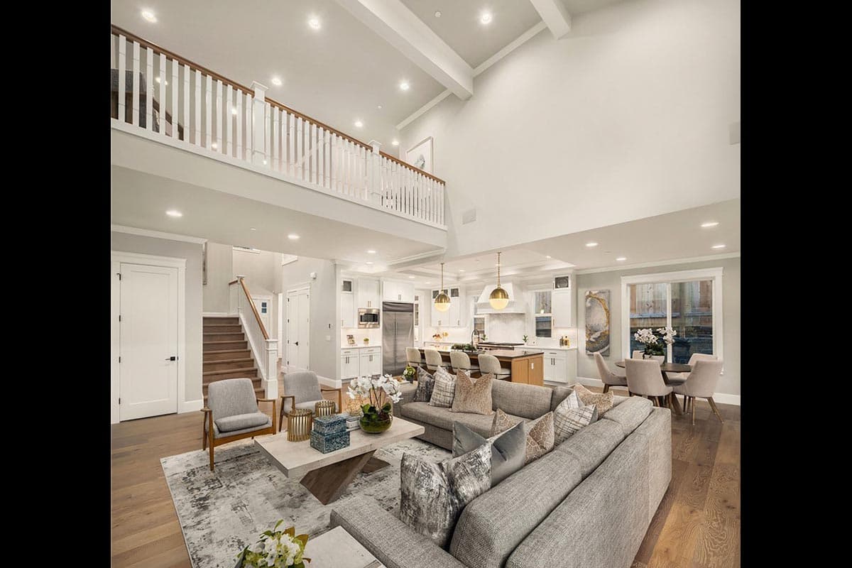 Interior view of a great room with vaulted ceiling, exposed beams, a lofted railing, stairs, and open kitchen.