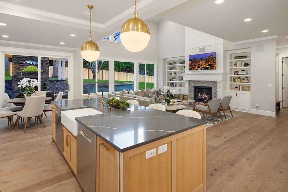 Open-concept living space with kitchen island, fireplace, built-in shelving, and large windows.