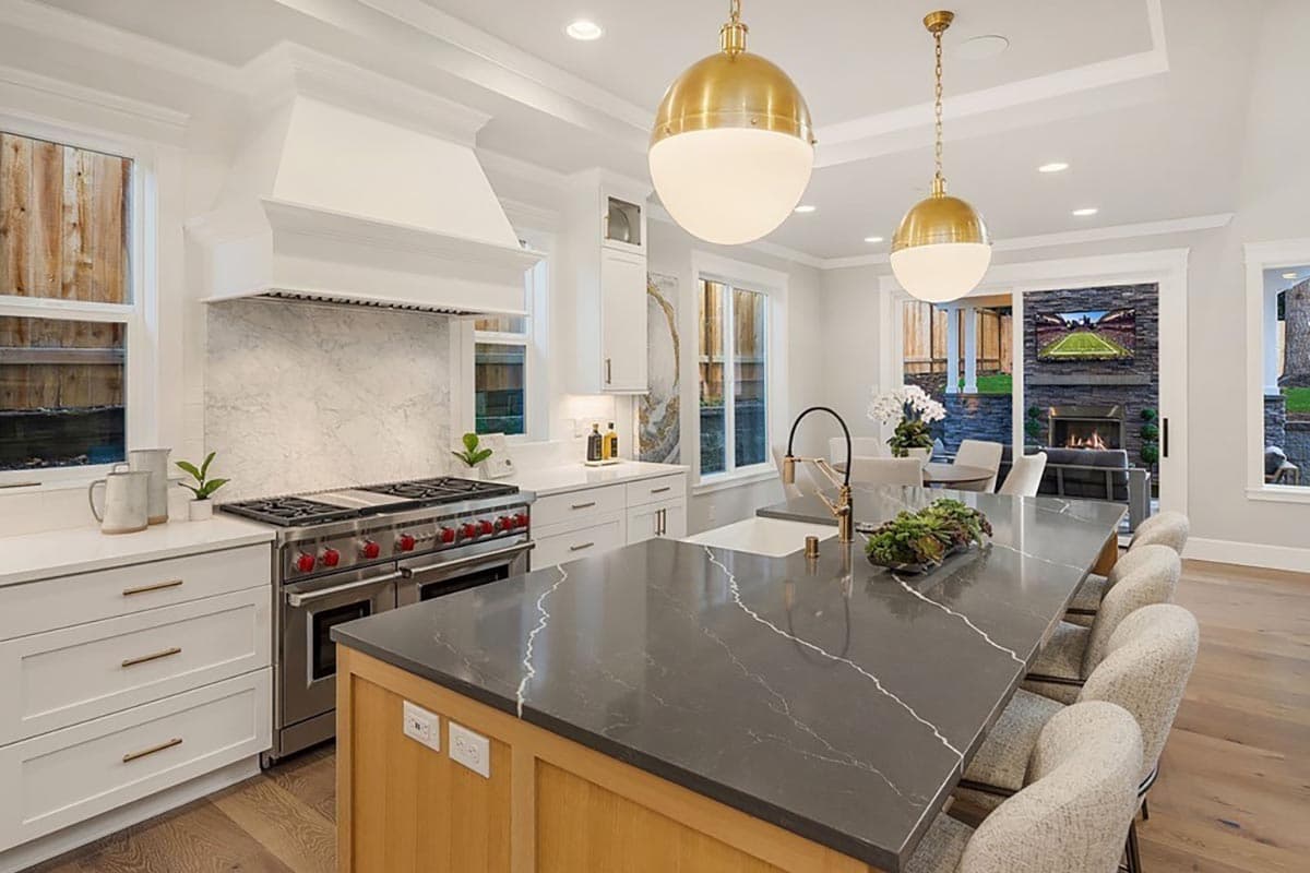 Kitchen with large island, waterfall countertops, stainless steel range, marble backsplash, and pendant lighting.