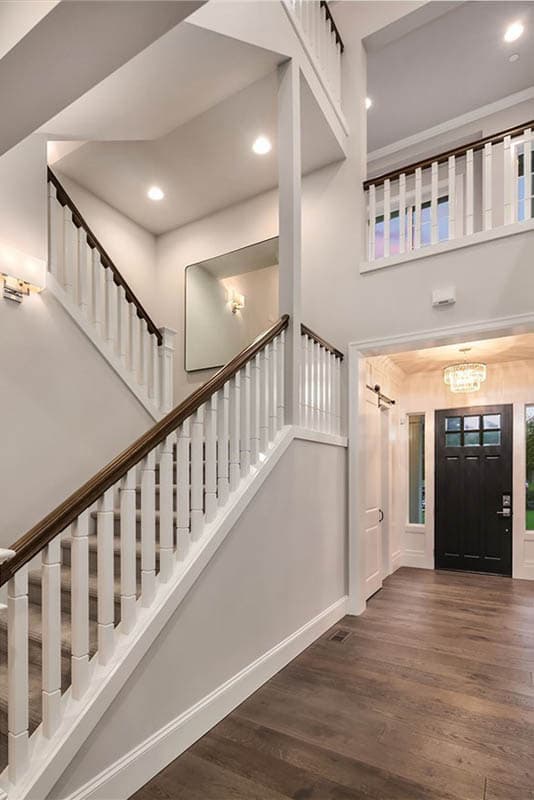 Interior view of a foyer with a grand staircase, dark-paneled front door, and hardwood floors.