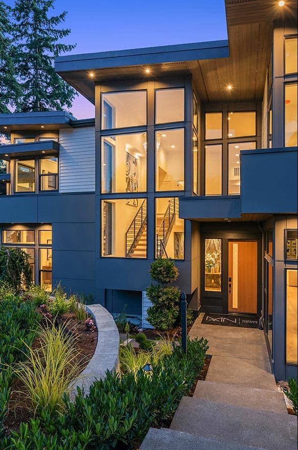 Modern house exterior with wood and gray siding, large windows, flat rooflines, and a wood front door.
