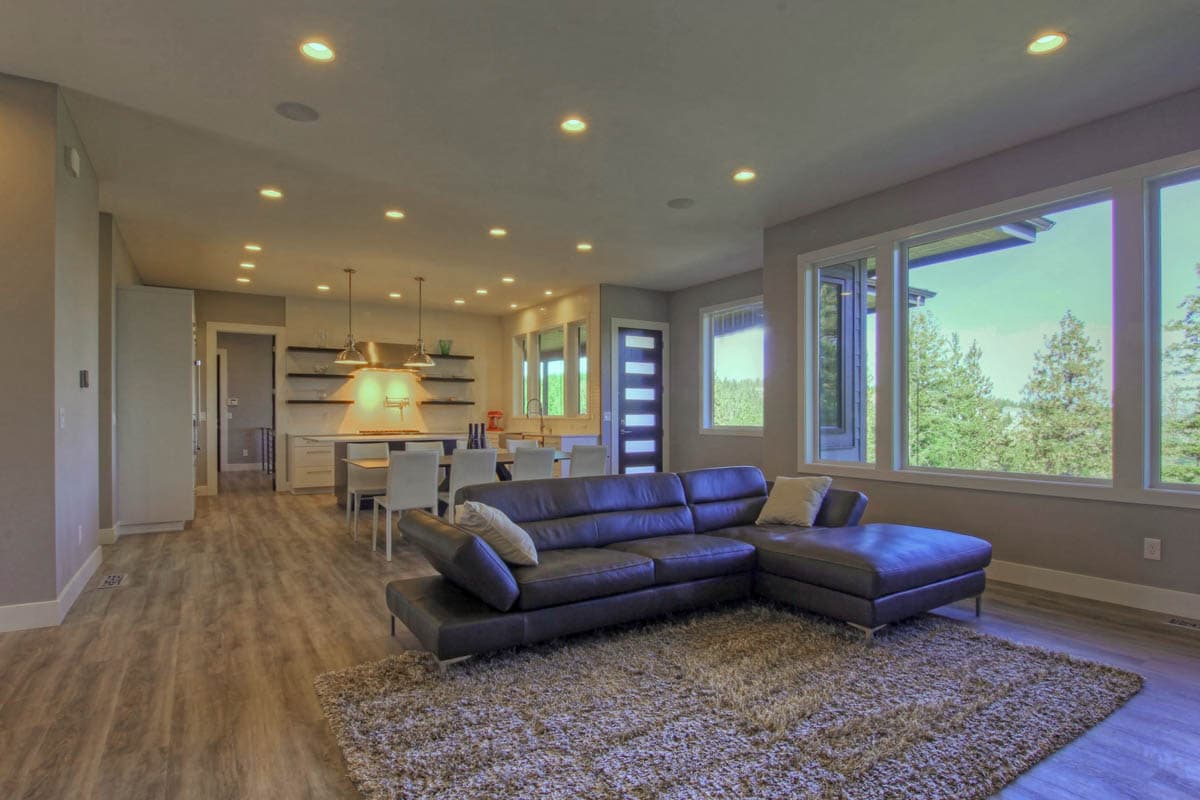 Modern open-concept living area with sectional sofa, large windows, and view of kitchen with island and dining table.