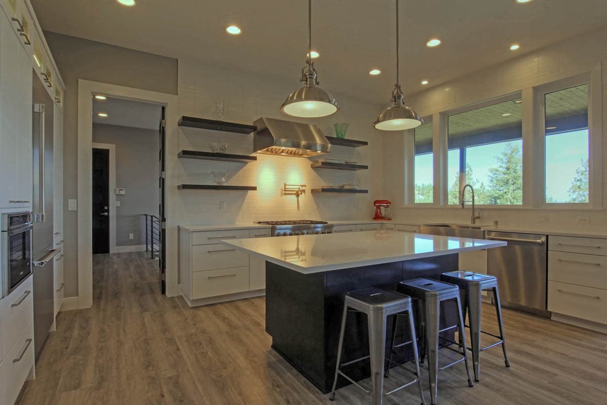 Contemporary kitchen with large island, stainless steel appliances, open shelving, and a wide window view.