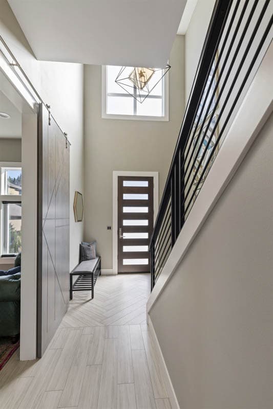 Modern foyer with a tall ceiling, barn door, sleek staircase, and a frosted glass front door.