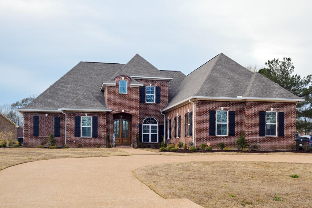 Two-story brick house plan exterior with arched entryway, multiple gables, dormer window, and black shutters.