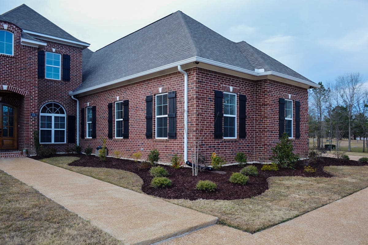 Exterior view of a brick house plan with black shutters, arched entryway window, and a pitched roof.