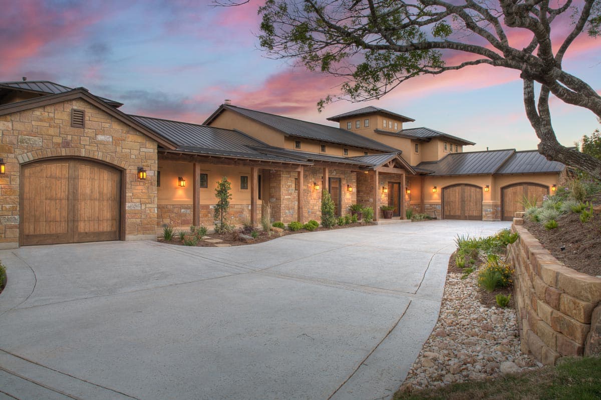 House plan exterior shows a multi-story home with stone accents, metal roof, covered porches, and multiple wood garage doors.