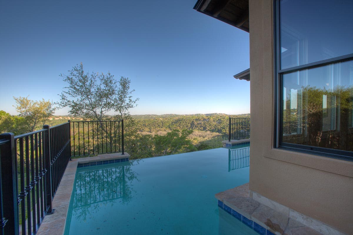 Modern house exterior with infinity pool, dark metal railing, and expansive hillside views.