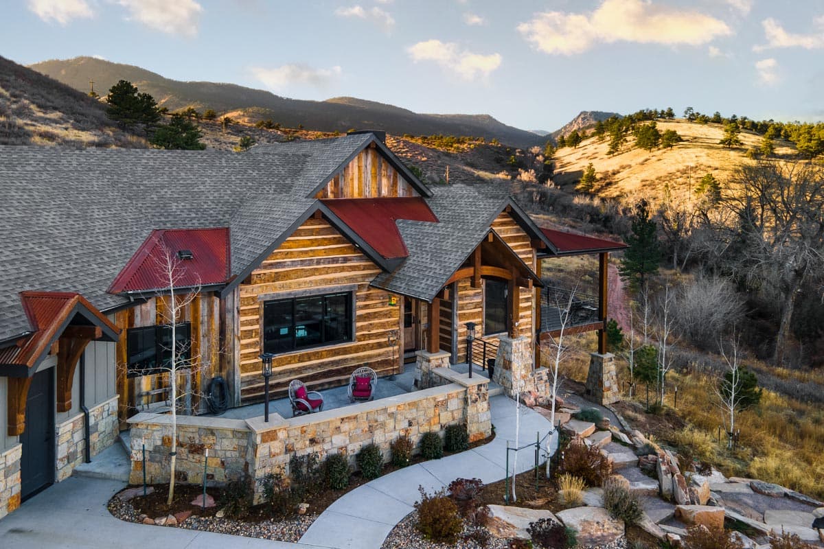 Log house plan exterior with stone accents, multiple gables, red metal roof, and covered porch.