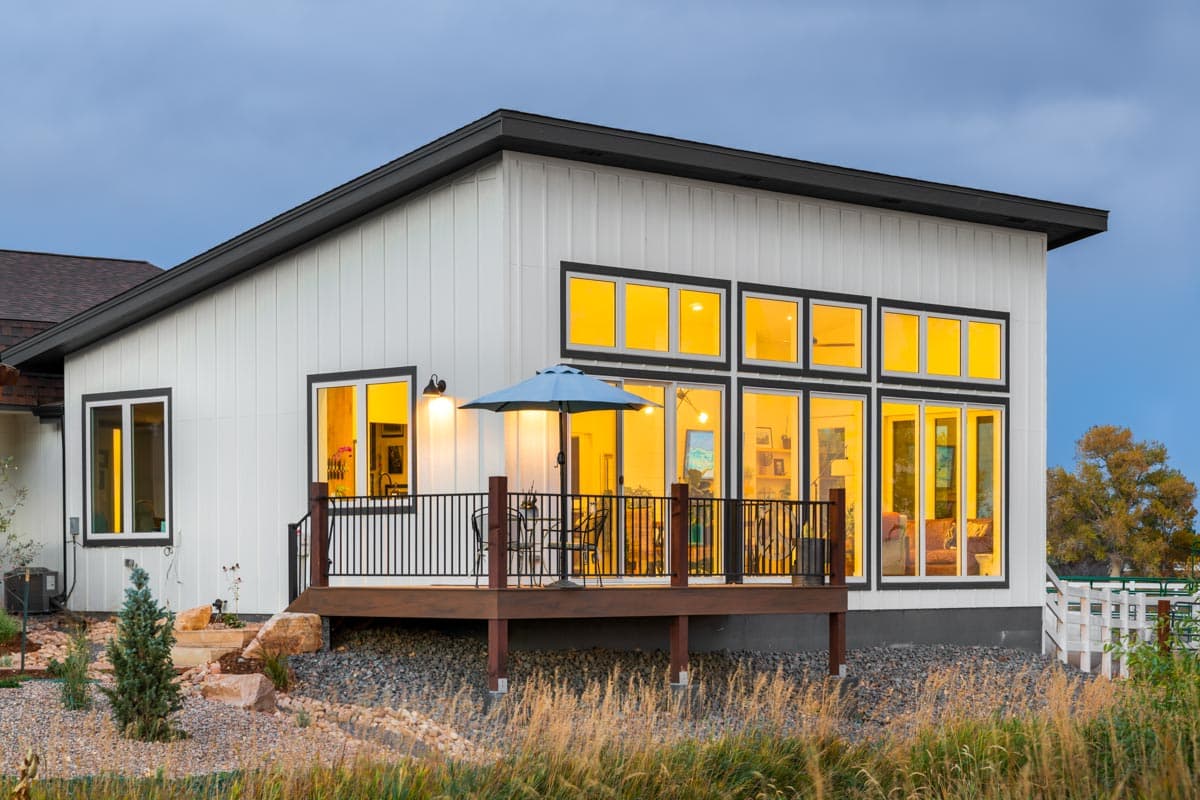 Modern house plan exterior with white vertical siding, large windows, and a dark-trimmed roof.
