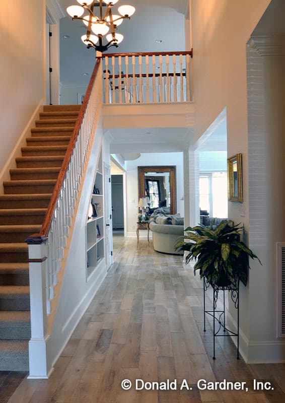 Interior view of a foyer with a staircase, open balcony, and living area visible. Wood-look flooring throughout.