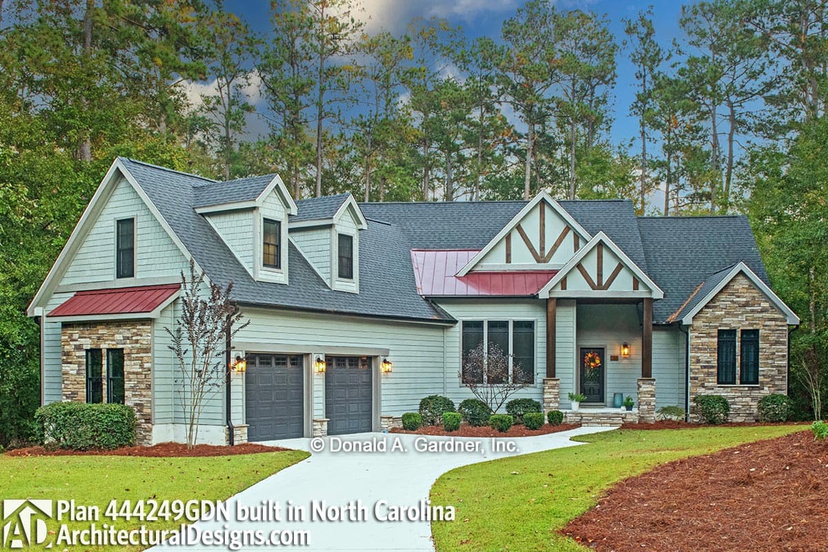 House plan exterior with Craftsman details, stone accents, metal roof dormers, and a three-car garage.